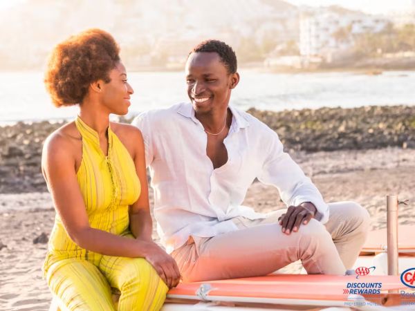 A smiling couple sits on a boat at the beach, enjoying a sunny moment together while chatting warmly.