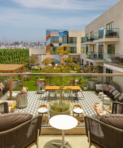 Sunny rooftop terrace with cushioned seating, small tables, and a lounge area overlooking modern apartments and blue sky, outdoors.