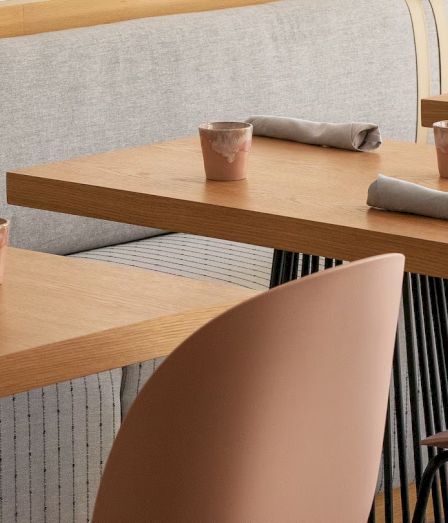 Cozy cafe scene with light wood tables, wrapped napkins, gray cups, and tan chairs. Simple, modern dining setup for guests.