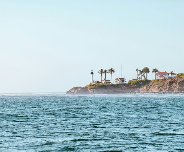 A distant coastline with a pier or small building on the horizon, meeting calm blue sea under a clear sky.