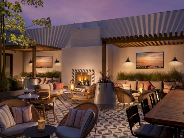 A stylish outdoor lounge with a fireplace, comfy seating, warm lighting, and geometric tiled floor. ￼