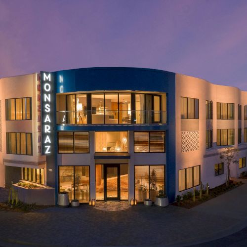 A modern, two-story office building with a curved facade, illuminated sign reading &ldquo;MONSARA7Z&rdquo; at night, glass entry doors, and warm interior lights.