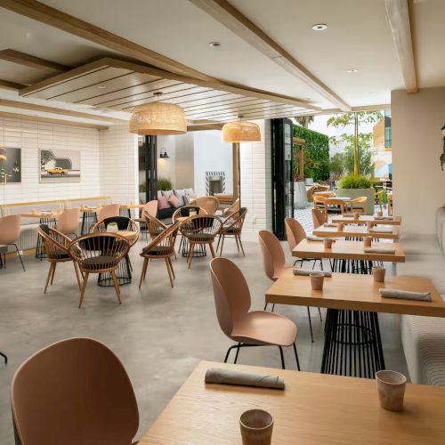 A bustling caf&eacute; or kitchen area with bar seating, warm lighting, and people dining; a person on a bicycle is visible in the background, suggesting a trendy, urban eatery.