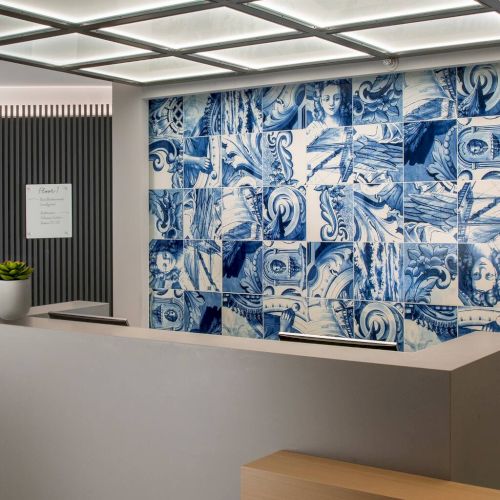 A modern classroom or meeting room with a long wooden desk, blue patterned wall art, a chalkboard on the left, and soft overhead lighting.