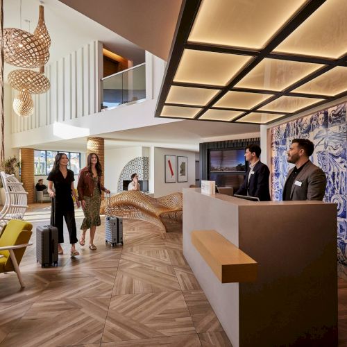 People walking through a bright, open indoor space with wooden beams, tables, and displays along the walls, creating a casual gallery or cafe vibe.