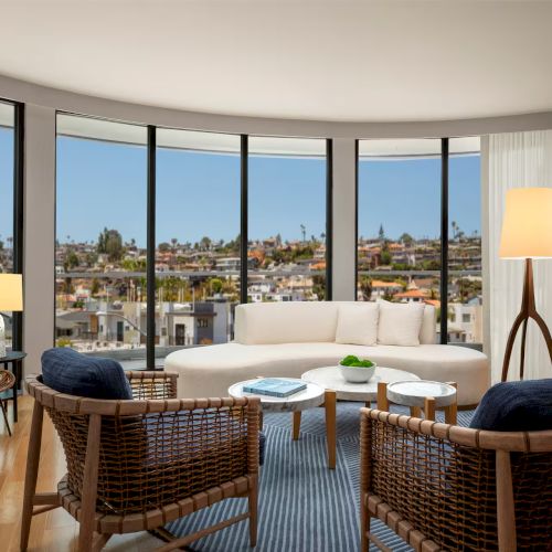 A bright hotel lobby with a modern seating area, large windows, and a city view; cozy sofas, planters, and warm lighting, inviting ambiance.